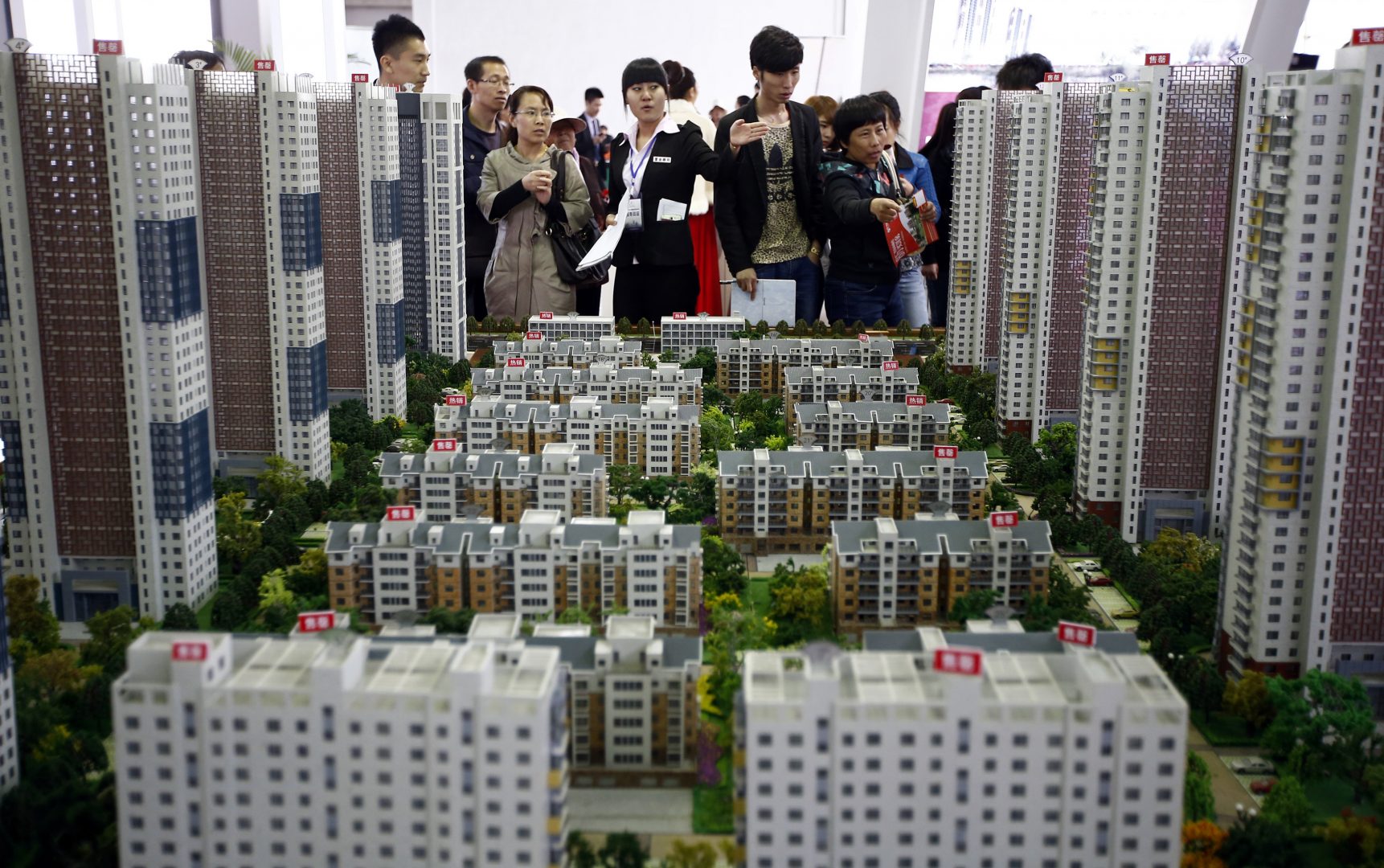 A sales assistant talks to visitors in front of models of apartments at a real estate exhibition in Shenyang, Liaoning province April 17, 2014. China's real estate investment rose 16.8 percent in first three months of 2014 from a year earlier, and revenues from property sales dropped an annual 5.2 percent, the National Bureau of Statistics said on Wednesday. REUTERS/Stringer (CHINA - Tags: REAL ESTATE BUSINESS) CHINA OUT. NO COMMERCIAL OR EDITORIAL SALES IN CHINA - RTR3LM1B